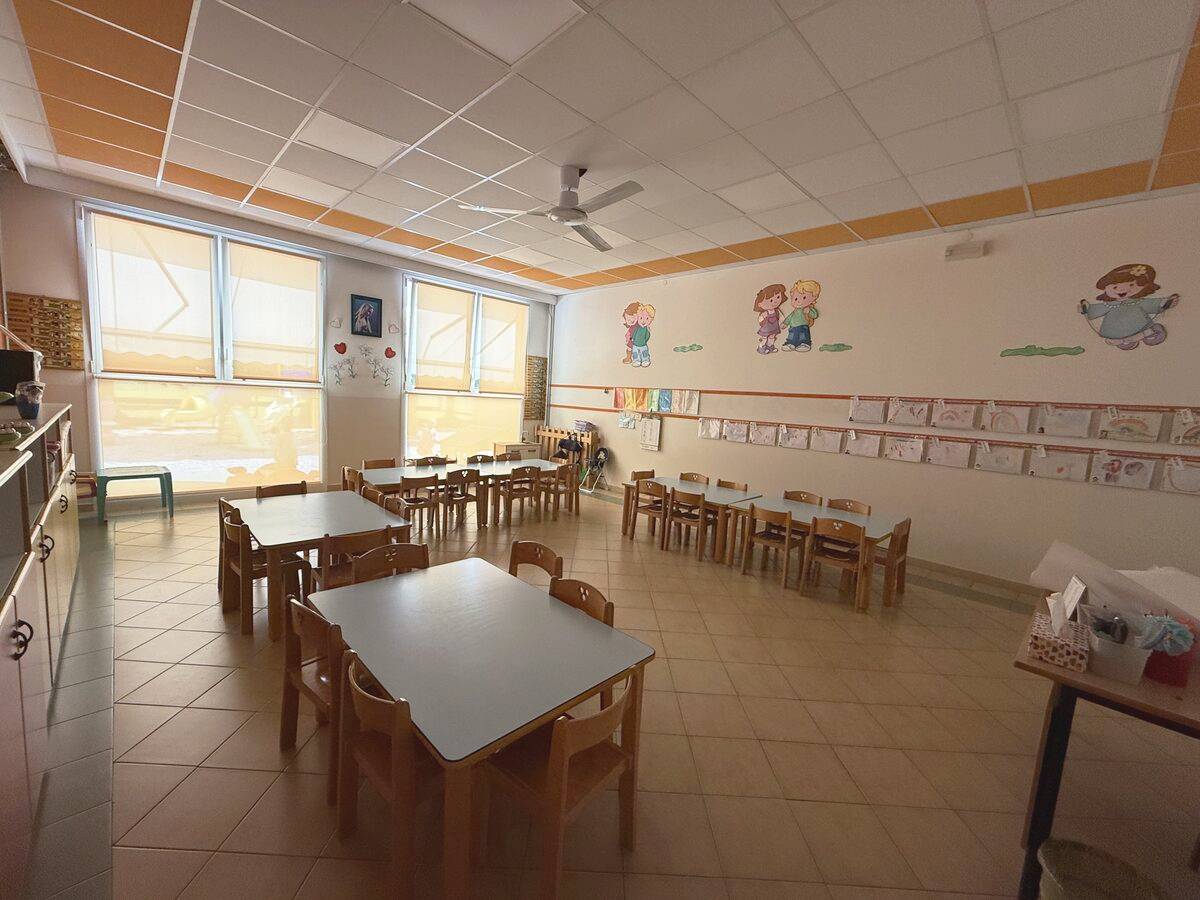 L'aula gialla con i tavolini, le sedie e i disegni dei bambini appesi alla parete