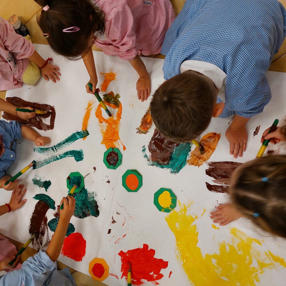 Bambini che dipingono insieme con i pennelli su un grande foglio