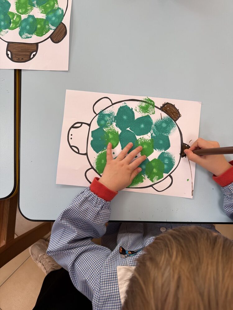 Bambino che colora con stampe verdi il guscio di una tartaruga disegnata