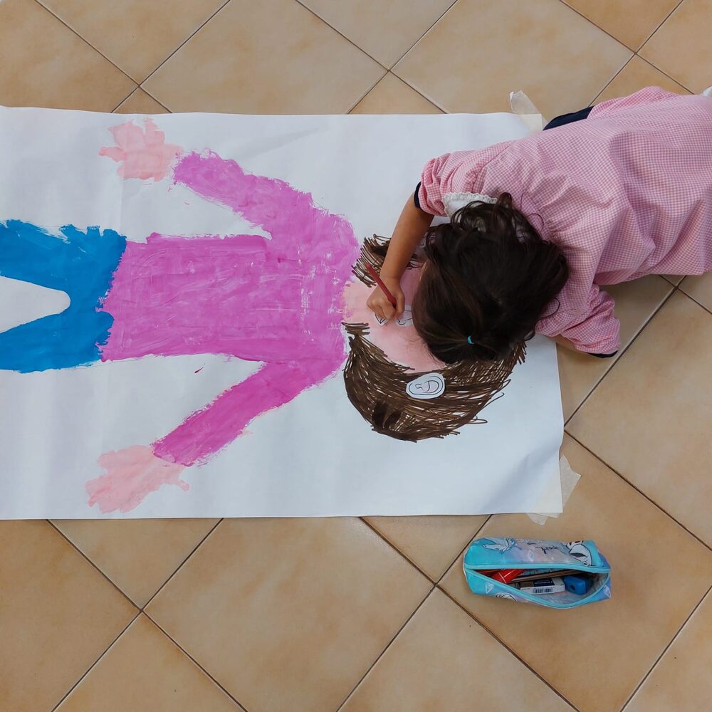 Bambina che disegna da sola la propria sagoma su un grande foglio
