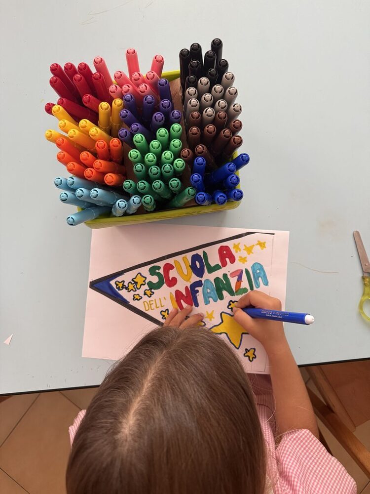 Bambina che colora con i pennarelli la scritta "Scuola dell'infanzia"